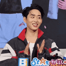 a man in a black and red jacket is smiling in front of a sign that says star hello asian
