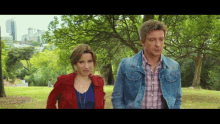 a man and a woman walking in a park with trees in the background