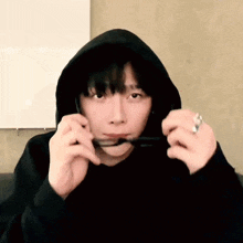 a man in a black hoodie is holding a pair of glasses in his mouth