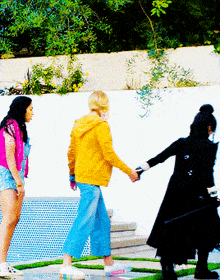 a woman in a yellow hoodie holds the hand of another woman in a black coat