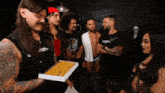 a man holding a box of cupcakes in front of a group of people