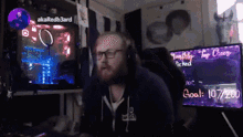 a man wearing headphones stands in front of a monitor that says goal 10/7/200 on it
