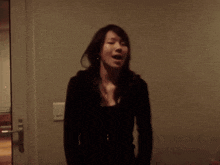 a woman in a black shirt is standing in front of a wall with a light switch on it