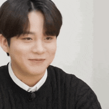 a man wearing a black sweater and a white shirt is smiling .