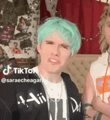 a man with green hair is making a funny face while sitting next to a woman .
