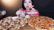 a woman is eating a slice of pizza next to two other pizzas on a table