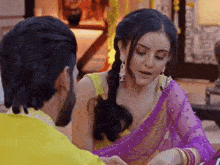 a man and woman are sitting next to each other and the woman is wearing a purple saree
