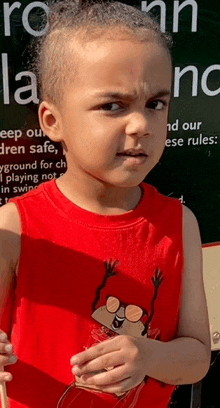 a young boy wearing a red tank top stands in front of a sign that says " keep our children safe "