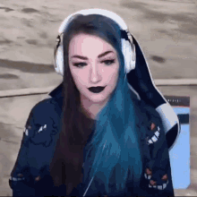 a woman with blue hair and black lipstick is wearing headphones and looking at the camera .