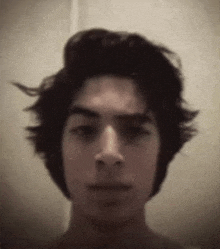 a young man with long hair is taking a selfie with his hair blowing in the wind .