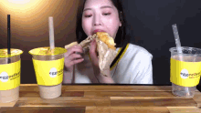 a woman eating a sandwich in front of three cups that say eggcellent