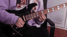 a man wearing a purple hoodie is playing an electric guitar