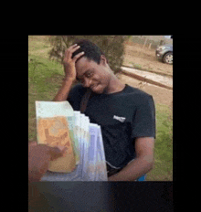 a man in a black shirt is holding a bunch of money in his hand