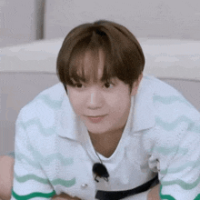 a young man in a green and white shirt is making a funny face while sitting on the floor .