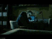 a joker is sitting at a desk in front of a laptop computer
