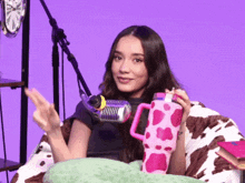 a woman is sitting in front of a microphone holding a cow print mug