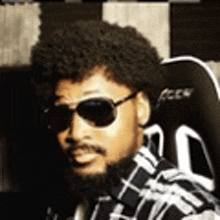 a man with a beard wearing sunglasses and a plaid shirt is sitting in a chair .