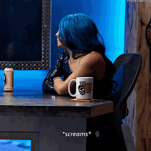 a woman with blue hair is sitting at a desk with a broken skull mug on it