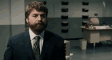 a man with a beard wearing a suit and tie is standing in a room .