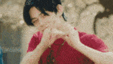 a young man in a red t-shirt is making a heart shape with his hands .