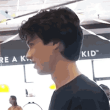 a young man in a black shirt stands in front of a sign that says " re a kid "