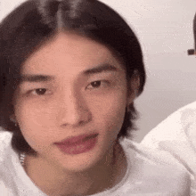 a close up of a young man with long hair wearing a white shirt and earrings .