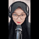 a woman wearing headphones and a hijab looks into a microphone with the starmaker app on her phone