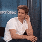 a man in a white t-shirt is sitting in a chair with his hand on his face .