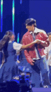 a man in a red jacket is dancing with a woman in a blue dress on stage .