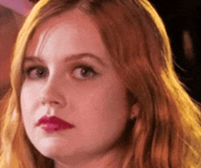 a close up of a woman 's face with long red hair and pink lipstick .