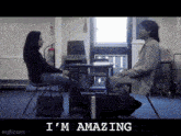 a woman sits at a desk talking to a man who is sitting in a chair with the words i 'm amazing below them
