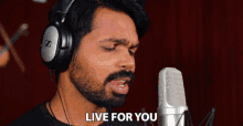 a man wearing headphones singing into a microphone with the words " live for you " written above him