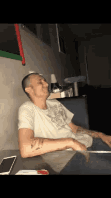a man with a tattoo on his arm sits at a table with his eyes closed
