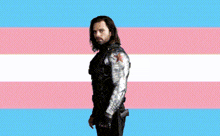 a man with a beard is standing in front of a transgender flag .