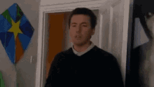 a man is standing in a doorway with a kite hanging on the wall behind him .