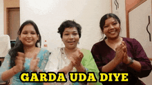 three women are clapping their hands in front of a sign that says garda uda diye
