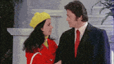 a man in a suit and tie stands next to a woman in a yellow hat