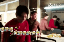 a man in a red shirt is standing next to another man in a room with chinese writing on the wall .