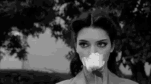 a black and white photo of a woman holding a white rose in her mouth .