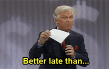 a man in a suit and tie is holding a piece of paper and says `` better late than ... '' .