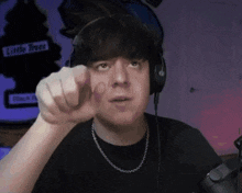a man wearing headphones points at the camera in front of a sign that says little tree