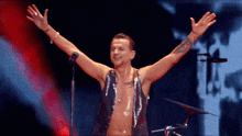 a shirtless man with his arms outstretched stands in front of a microphone