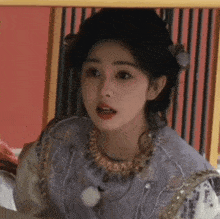 a woman wearing a purple dress and a gold necklace is sitting under a table .