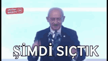 a man in a suit and tie is giving a speech in front of two microphones with the words simdi sictik written below him