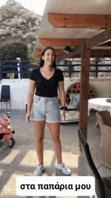 a woman wearing shorts and a black shirt stands in front of a sign that says " sta paparia mou "