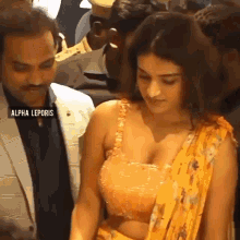 a woman in a yellow crop top and a yellow sari is standing next to a man in a suit .