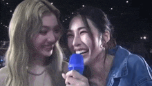 two women are laughing while holding a microphone and smiling .