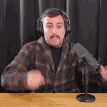 a man wearing headphones and a plaid shirt stands in front of a microphone ..