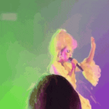 a woman in a white dress is singing into a microphone on a stage in front of a purple background .