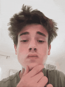 a young man with messy hair holds his hand to his chin and looks at the camera